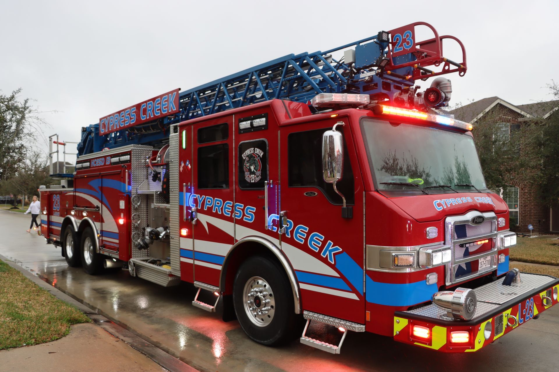 Red fire truck with ladder driving on a wet street in a residential neighborhood