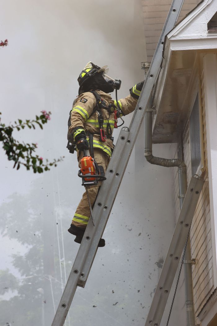 A fireman is on a ladder with a saw. 
