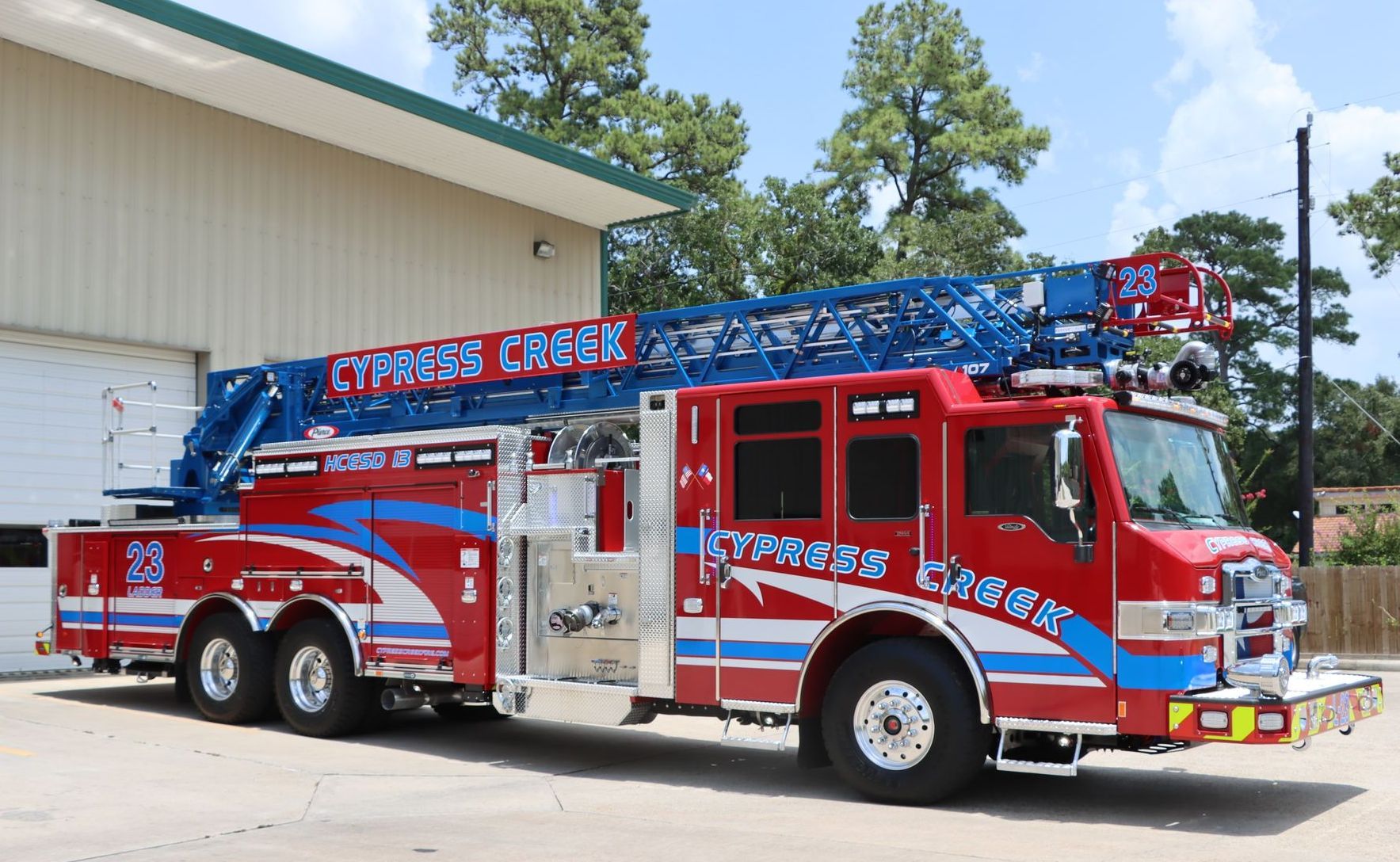 A red and blue fire truck is parked in front of a building. Cypress Creek Ladder Truck 23.