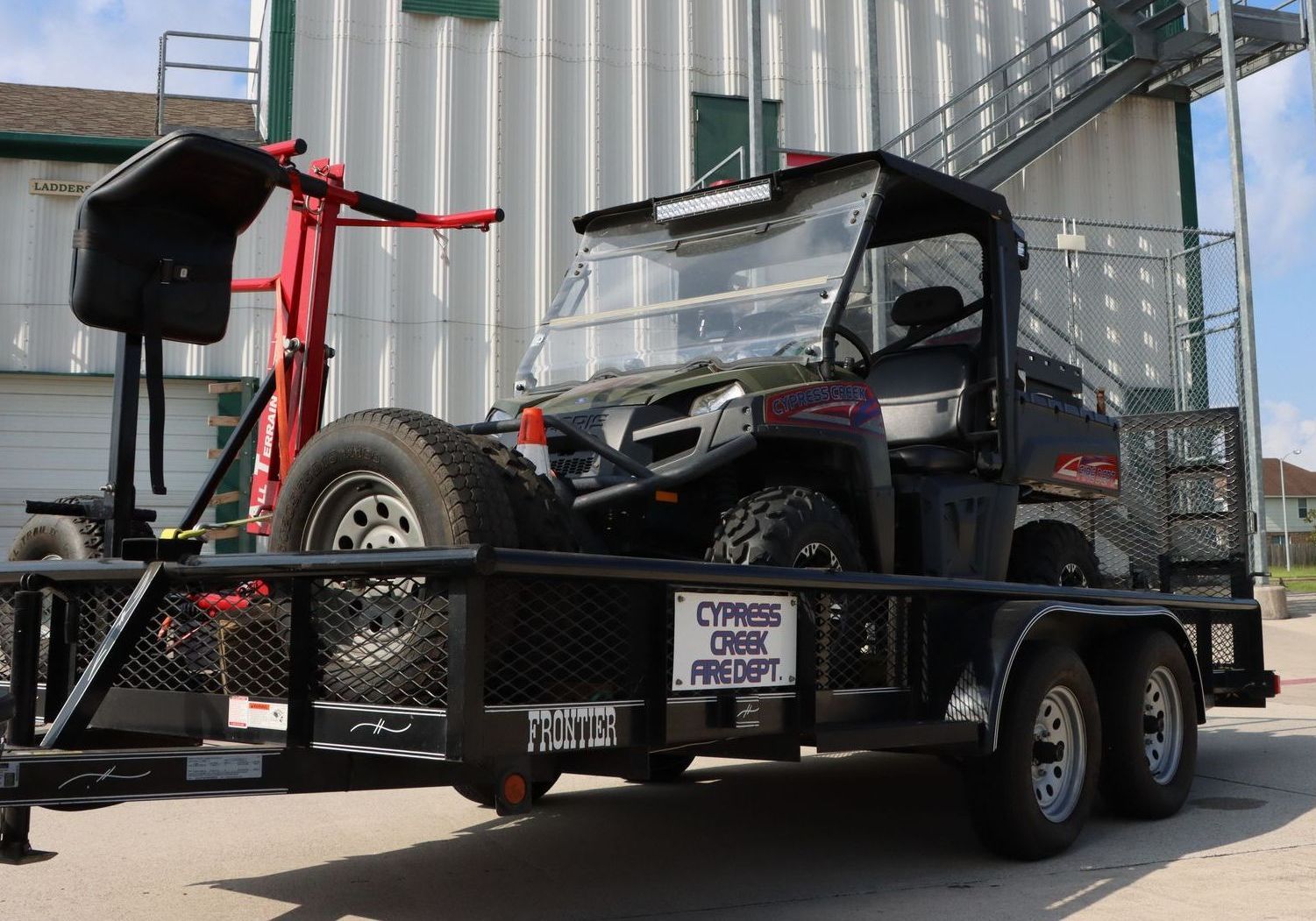 A trailer with a utility vehicle on it is parked in front of a building.