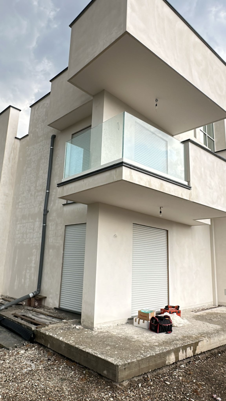 Esterno di una moderna casa bianca a due piani con balcone, ringhiera in vetro e materiali da costruzione sul patio anteriore.