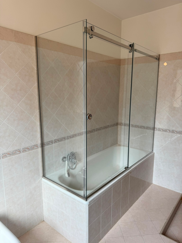 Cabina doccia con pareti in vetro, piastrelle beige e piatto doccia bianco.
