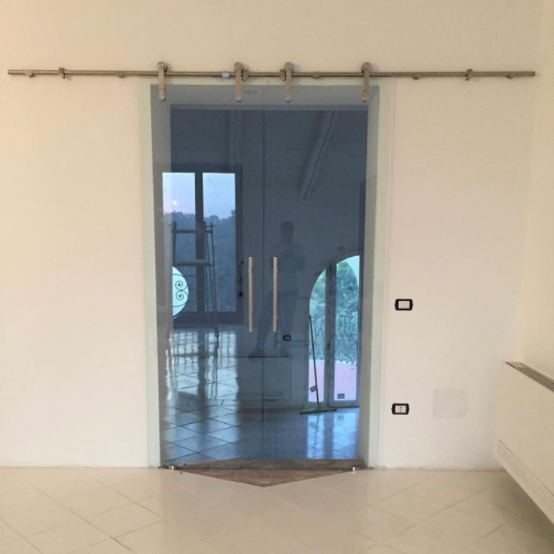 Stanza vuota con pareti bianche, pavimento piastrellato e porta a vetri con vista sull'esterno.