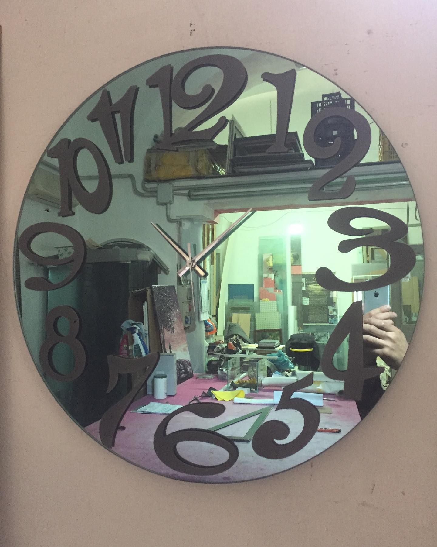 Orologio da parete rotondo nero con numeri sovradimensionati che riflettono una stanza disordinata e una persona che scatta la foto.