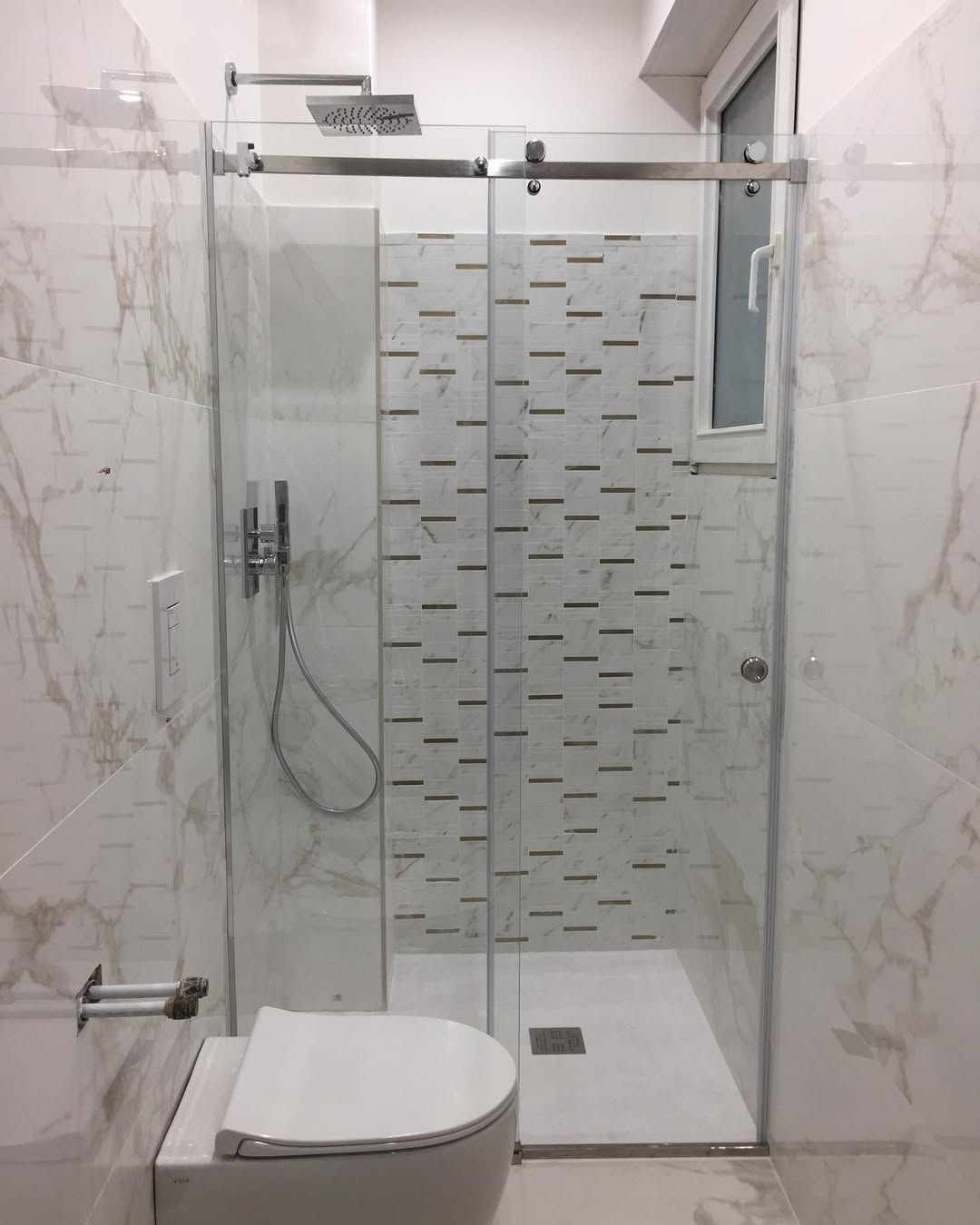 Bagno piccolo con doccia moderna in vetro, parete piastrellata, doccetta a mano e WC.