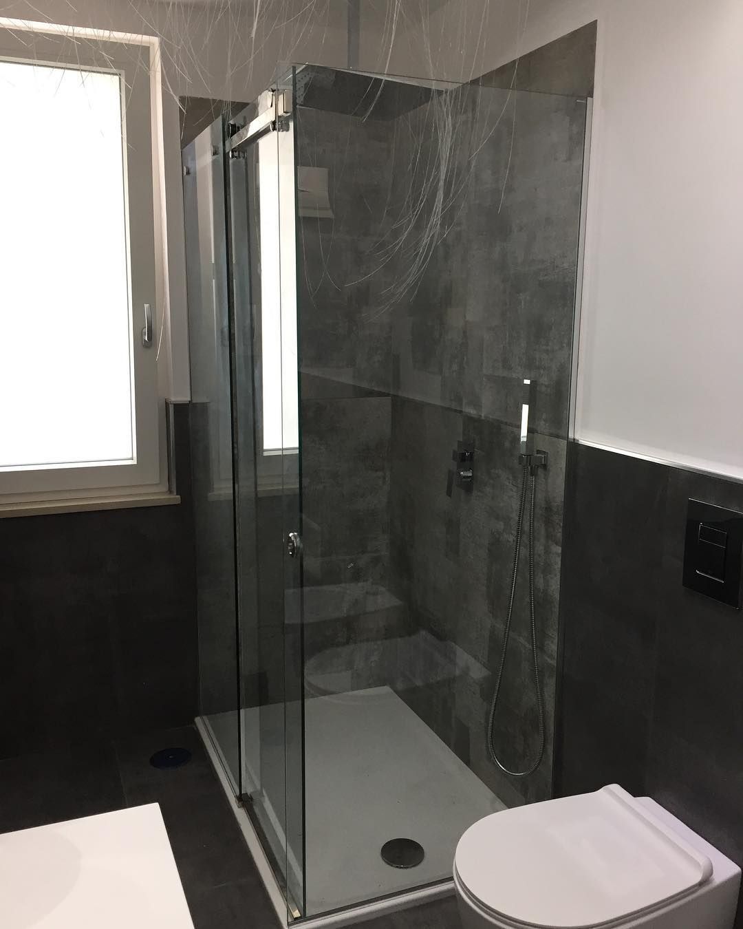 Bagno moderno con doccia in vetro, WC bianco e pareti rivestite con piastrelle bianche e nere.