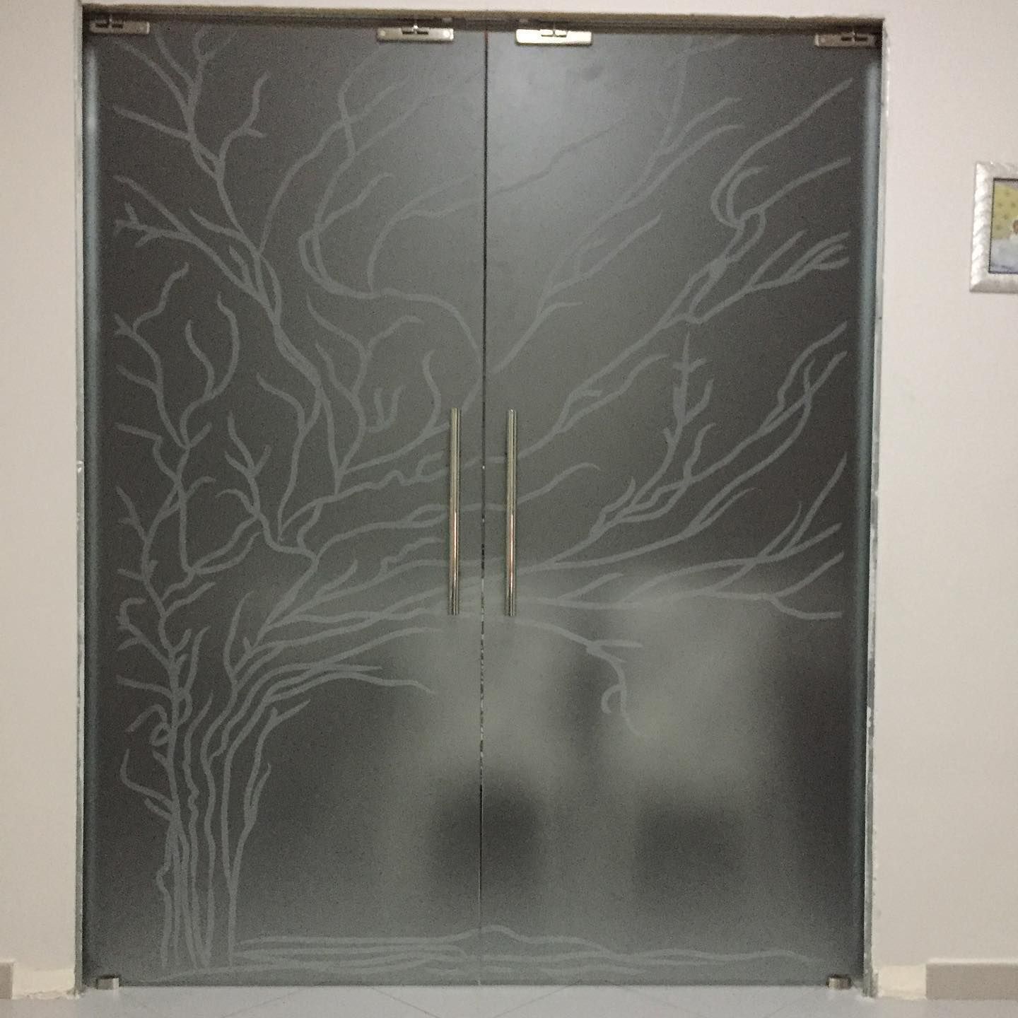 Doppie porte in vetro satinato con rami d'albero incisi e maniglie verticali in un corridoio