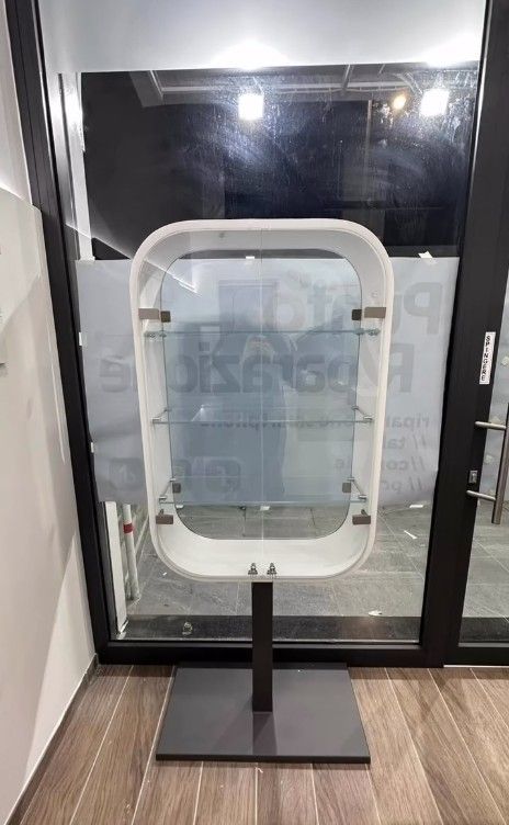 Specchio ovale bianco autoportante su supporto nero in una stanza moderna con porte a vetri e pavimento in legno.
