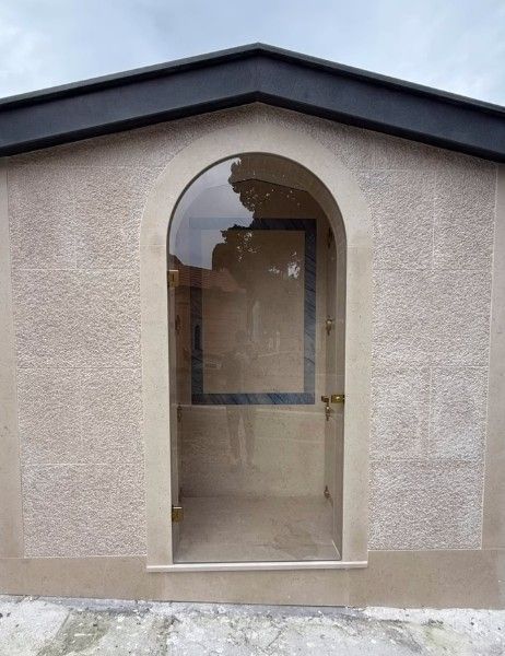 Porta d'ingresso ad arco in vetro su una parete in stucco beige con finiture del soffitto scure.
