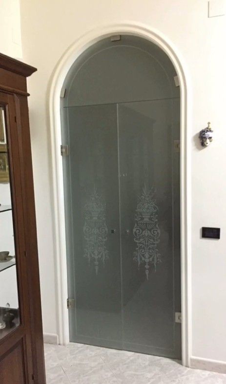 Porta ad arco in vetro satinato in un corridoio bianco, con decorazioni floreali incise.