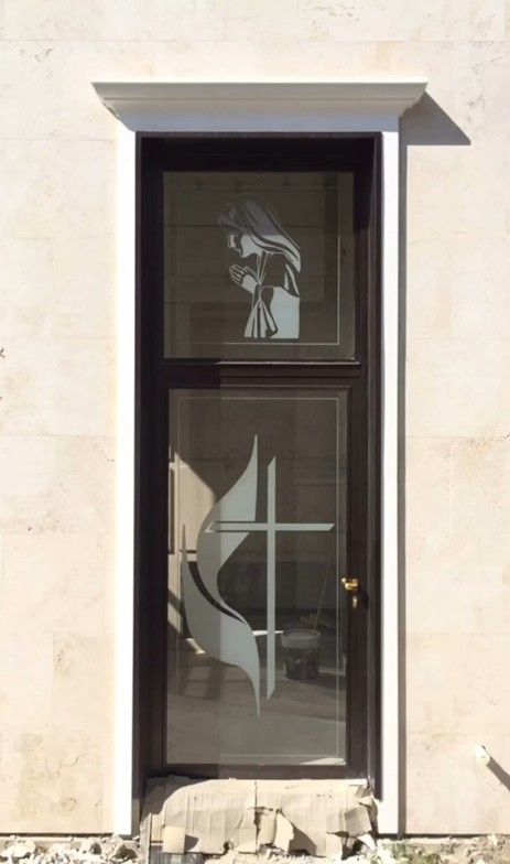 Porta d'ingresso in vetro con cornice scura incastonata in un muro di pietra chiara, che mostra un disegno decorativo satinato.