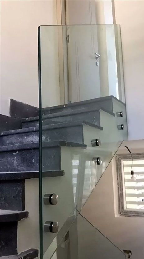 Ringhiera in vetro per le scale, gradini grigi e una piccola finestra in un interno moderno.