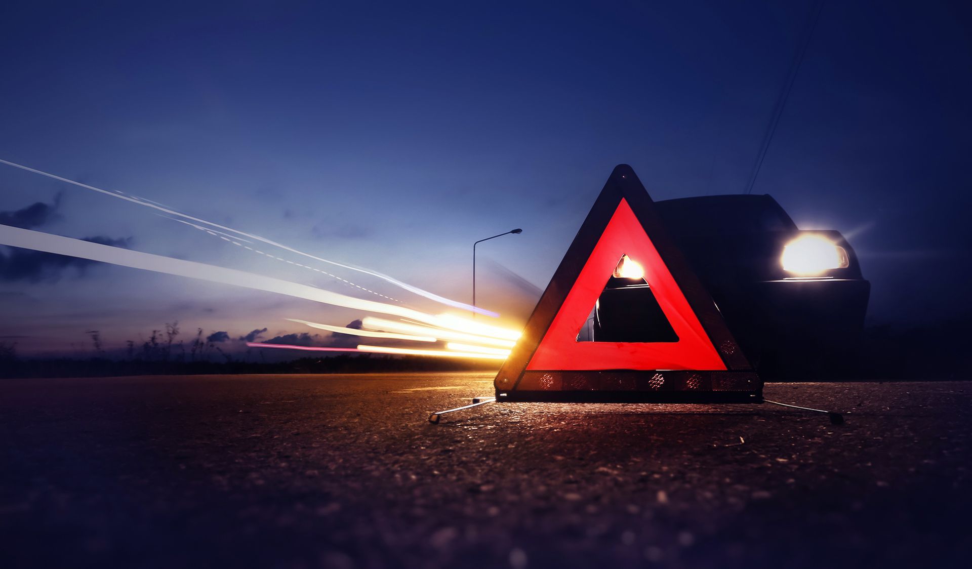 A car is driving past a red triangle on the side of the road.