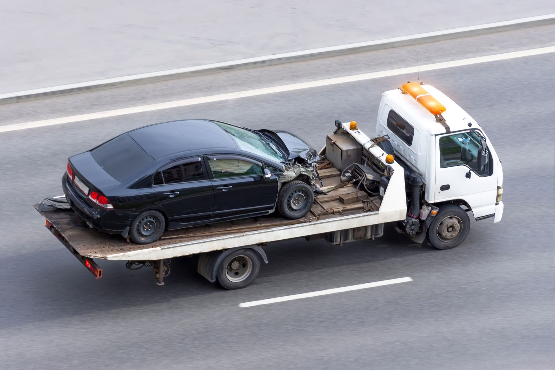 A tow truck is towing a black car on a highway.