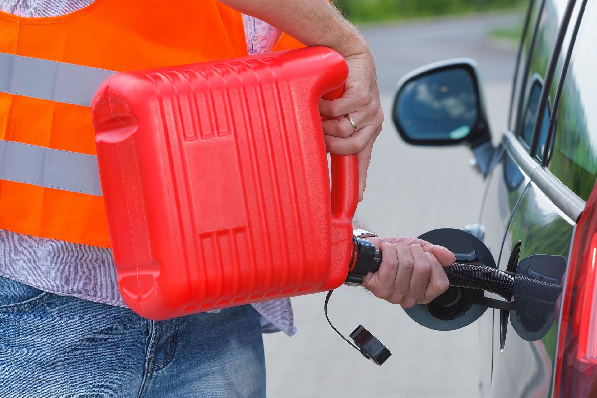 A person is holding a red gas can next to a car.