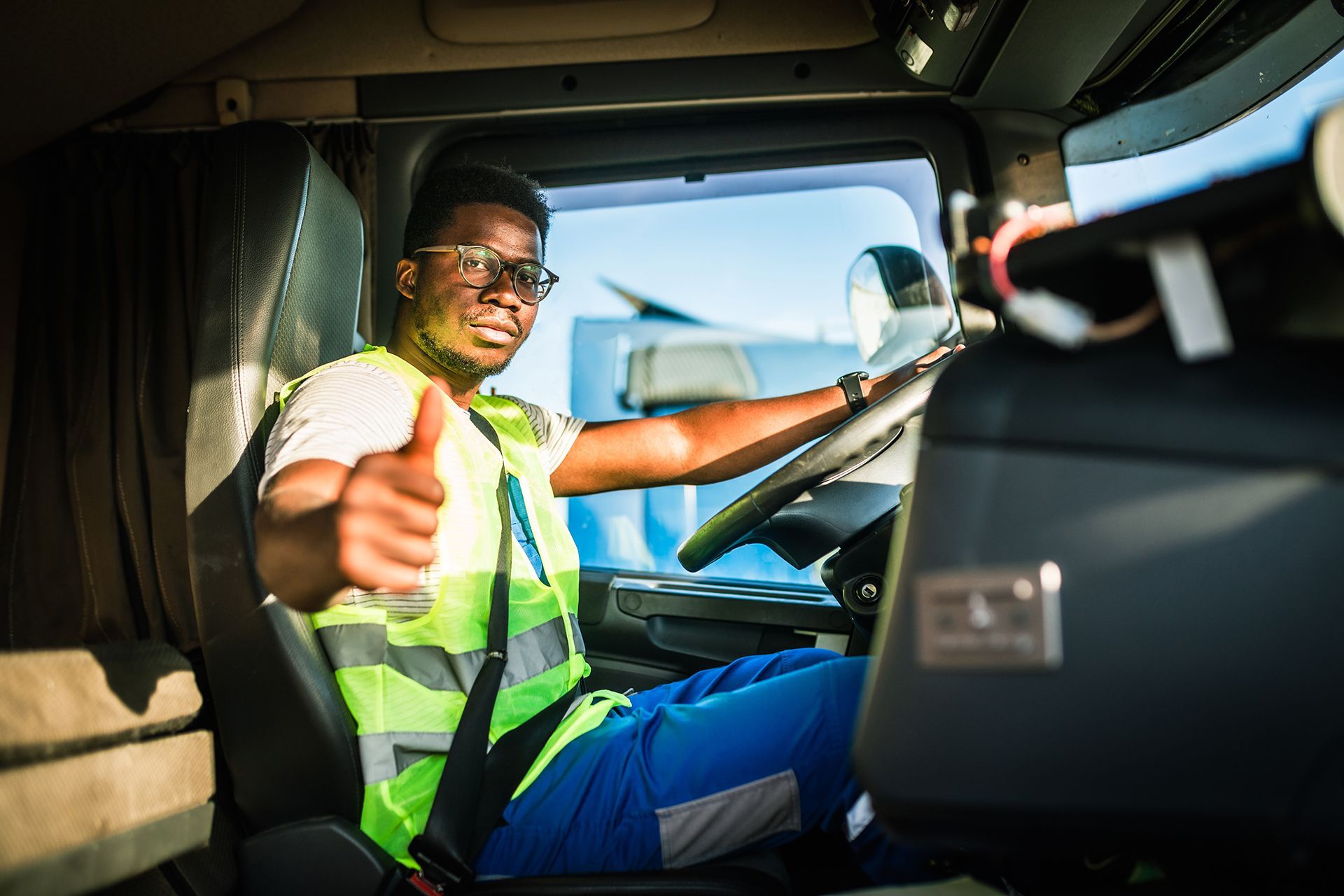 A man is sitting in the driver 's seat of a truck and giving a thumbs up.