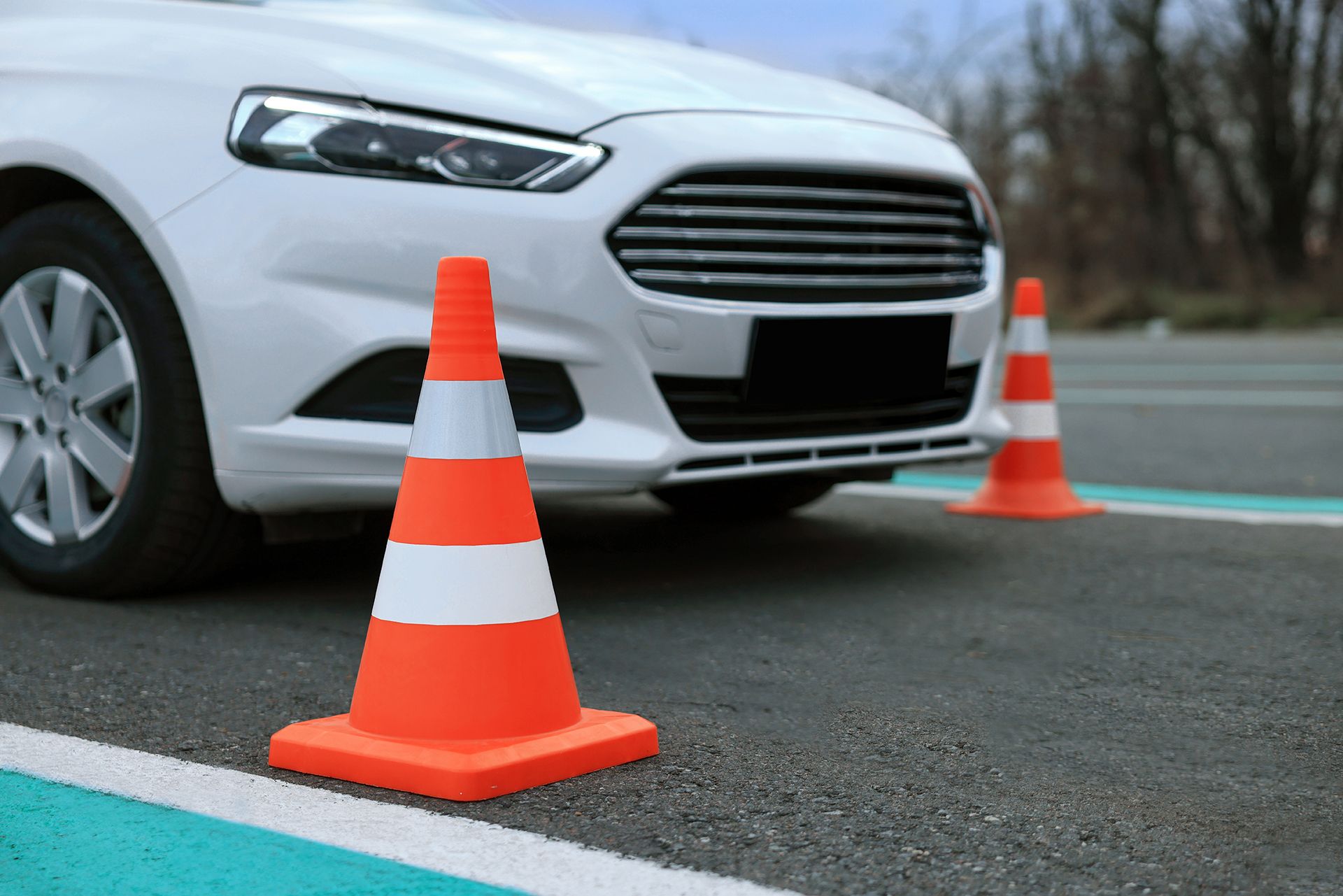 A white car is parked next to two orange and white traffic cones on the side of the road.
