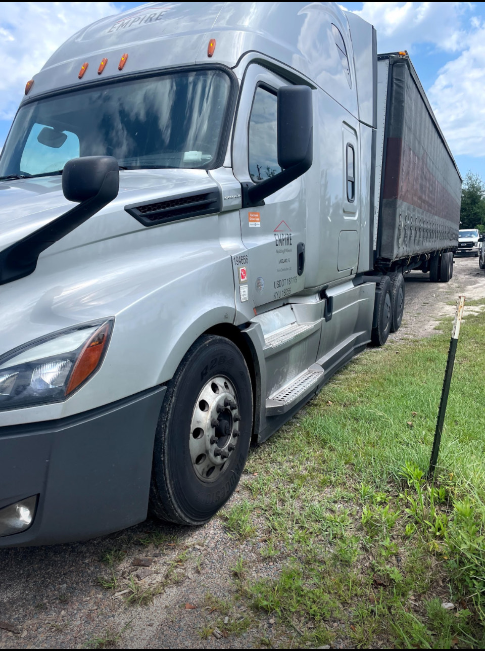 A semi truck with a broken windshield is parked in a grassy area.