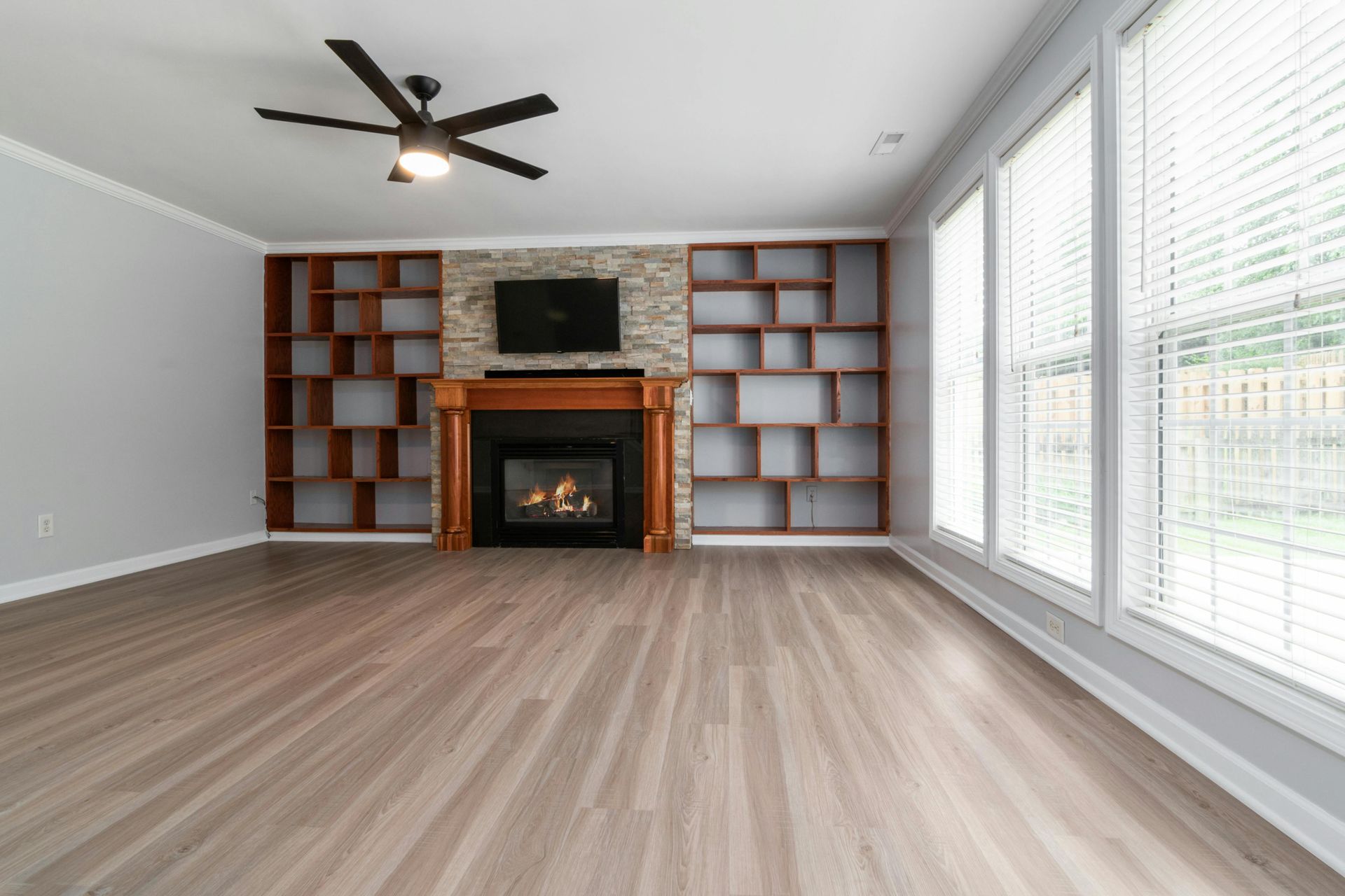 A person in jeans and a red plaid shirt installs wood-look laminate flooring panels on a gray underlayment.