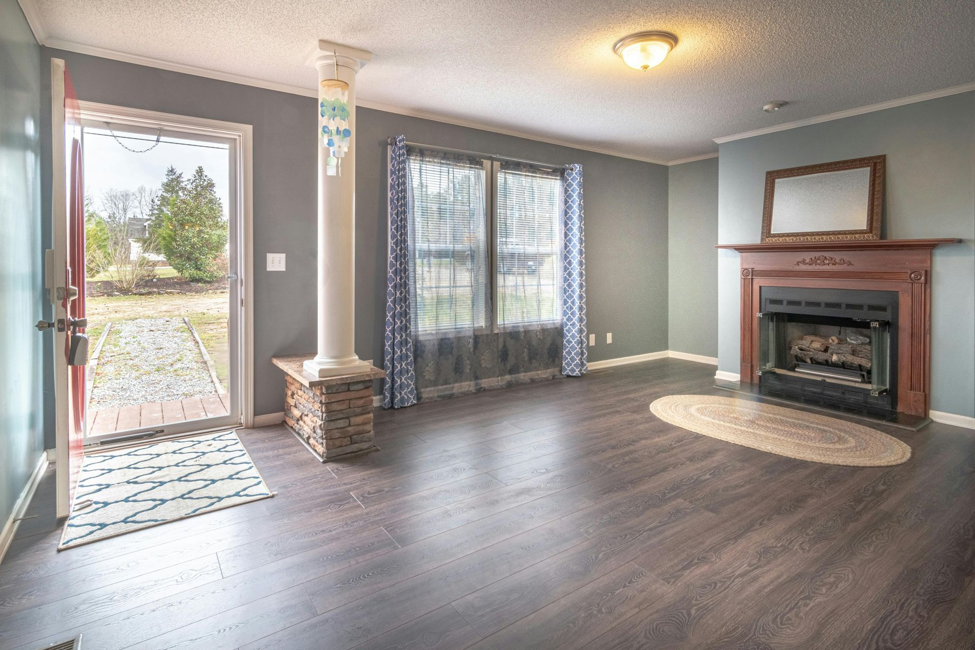 Empty living room with dark wood floors, gray walls, fireplace, and sliding glass door.
