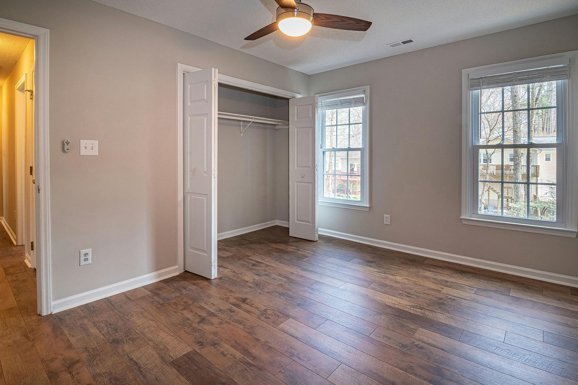 Empty bedroom with gray walls, wood floor, ceiling fan, closet, and two windows with white blinds