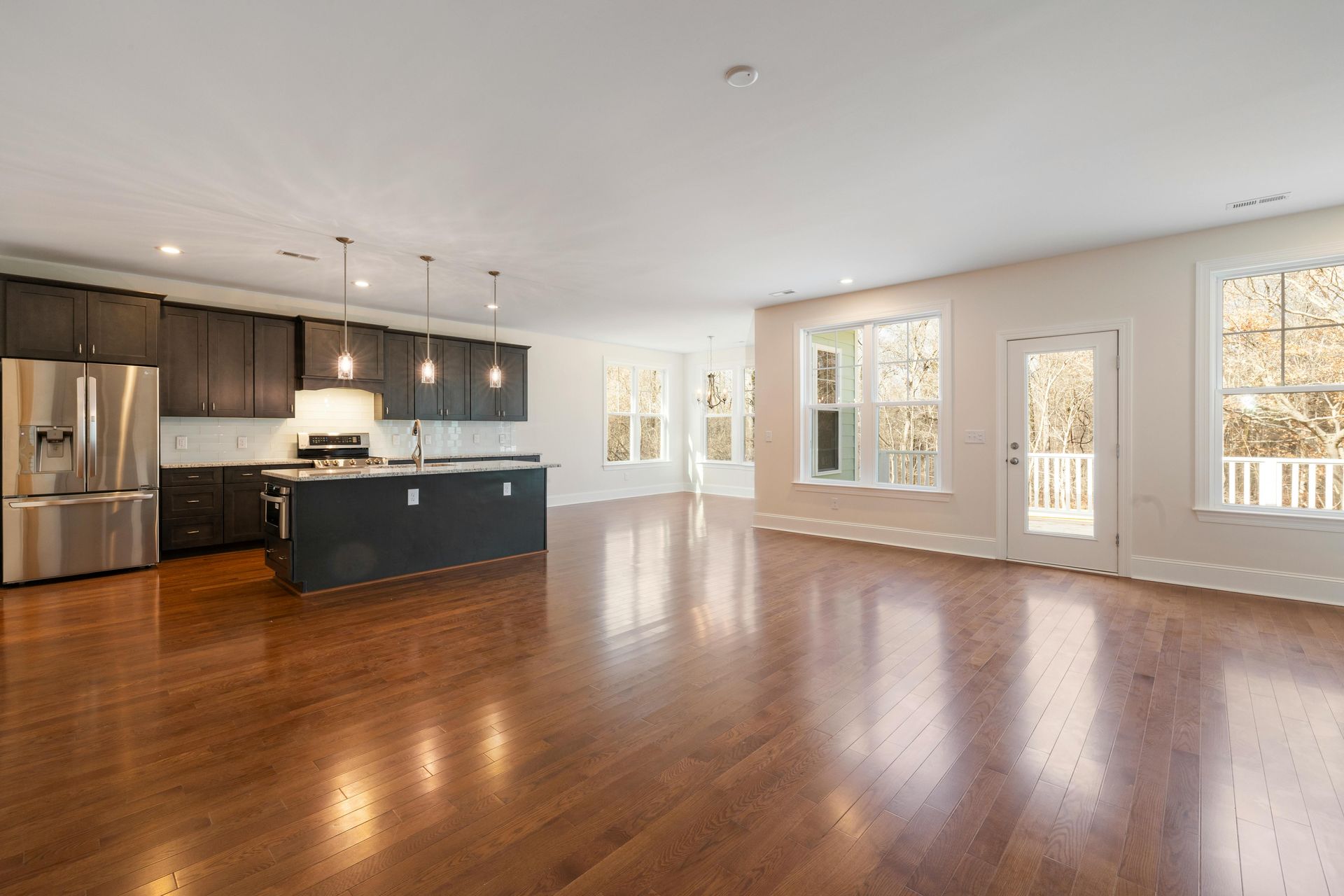 Spacious open-plan kitchen and living room with hardwood floors, dark cabinets, and large windows.