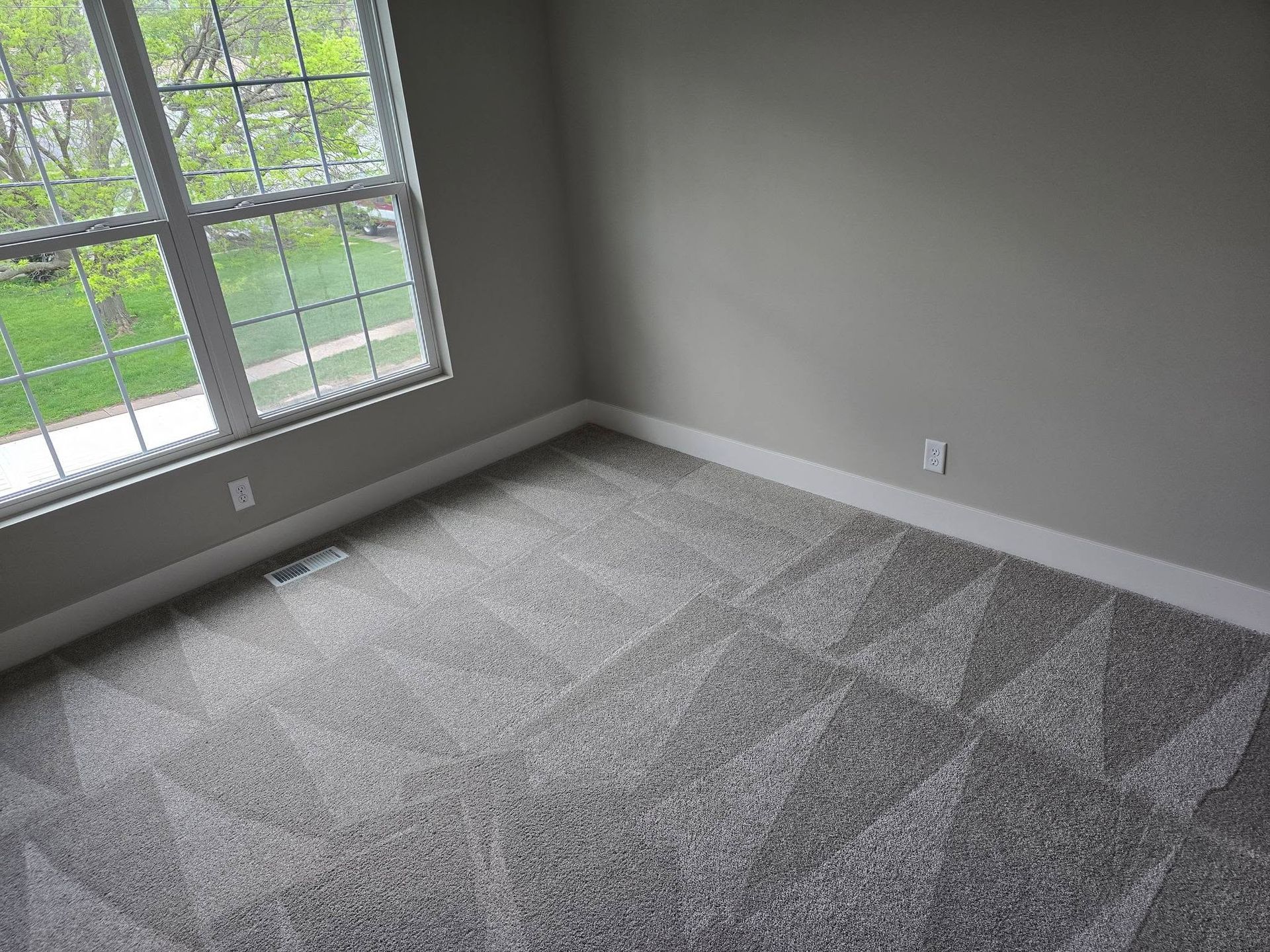 Empty gray-carpeted room with large window and light gray walls