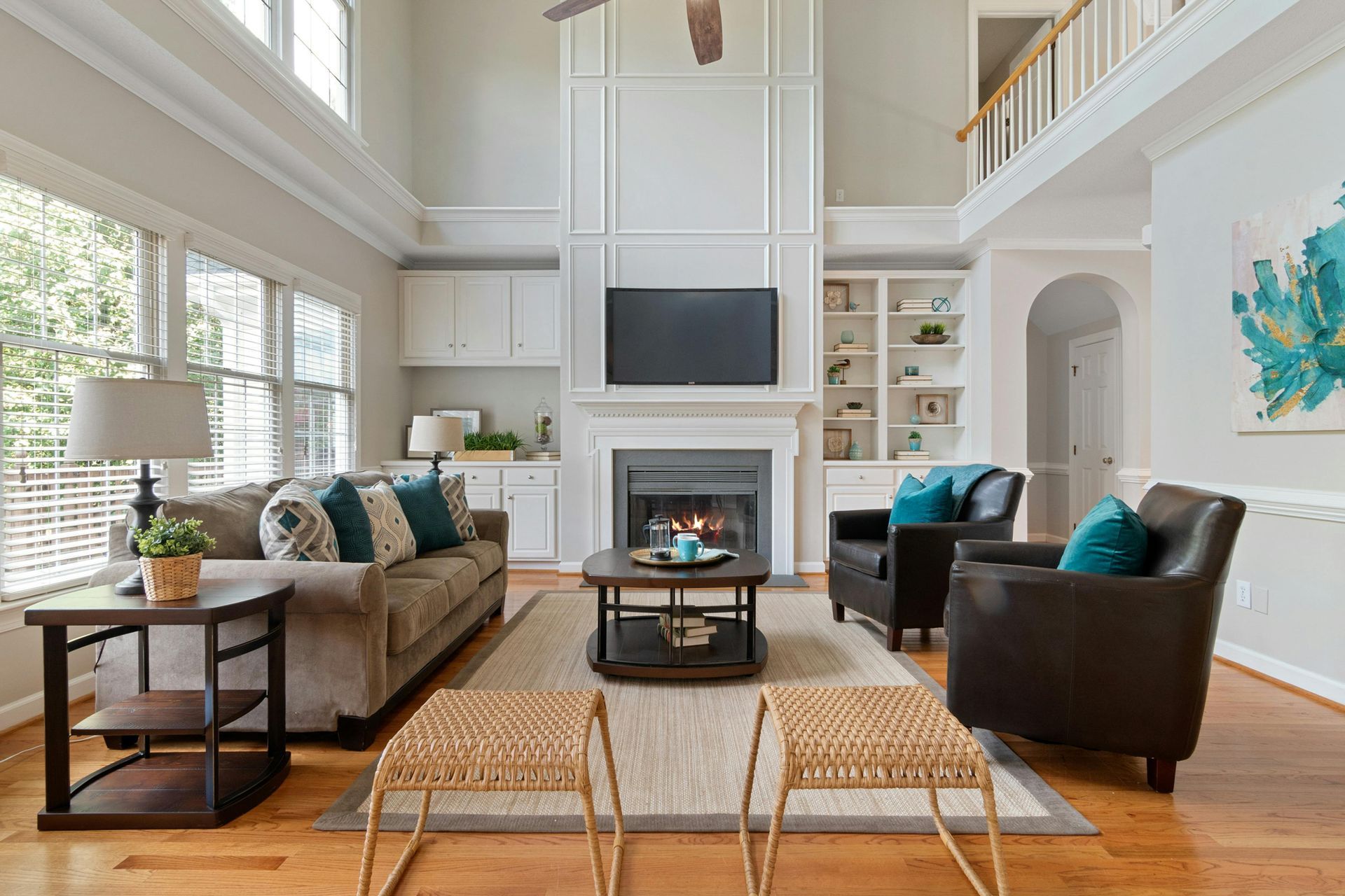 A modern living room with hardwood floors, a dark sofa, a coffee table, and large windows overlooking autumn trees.