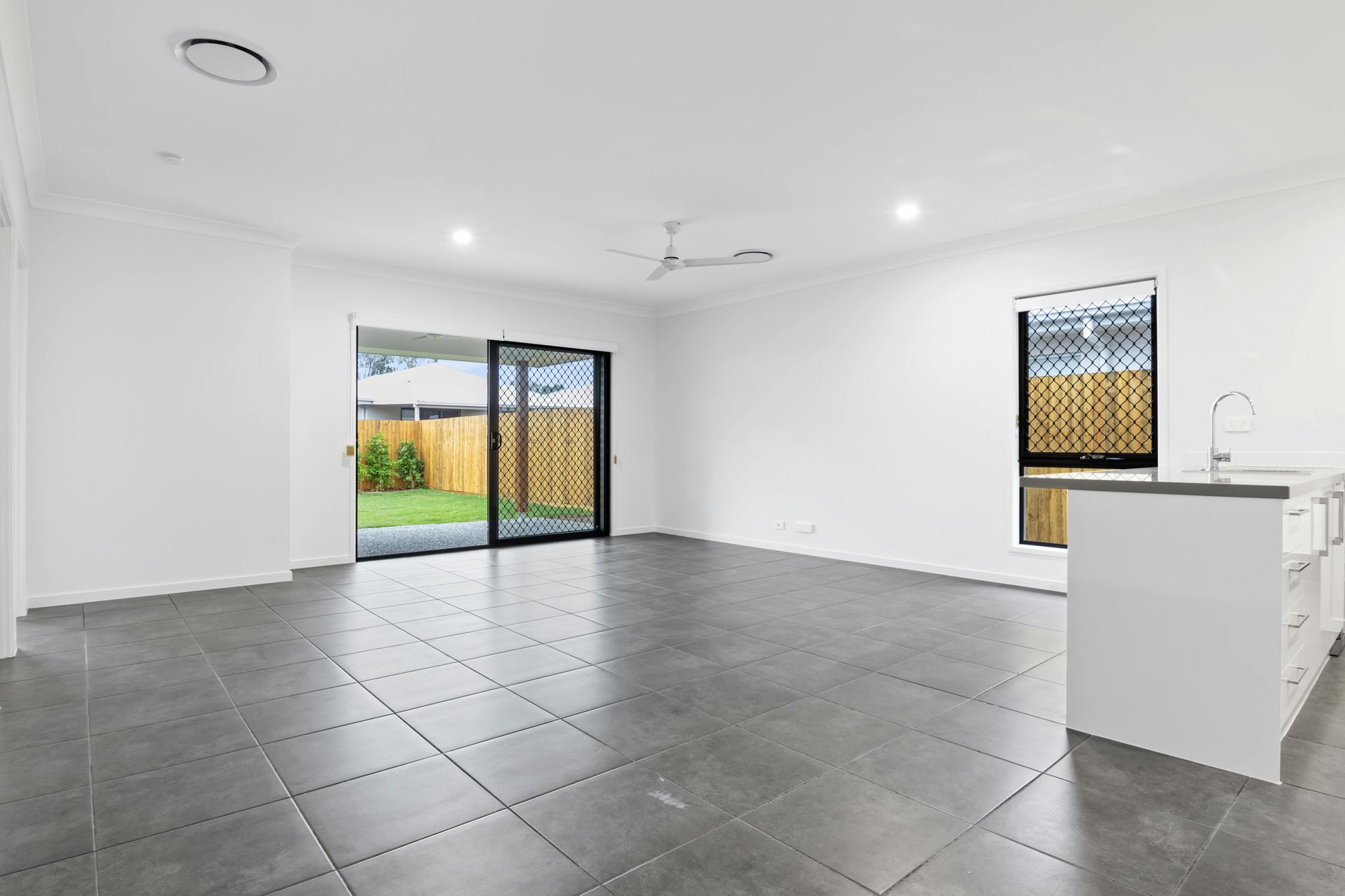 Empty modern living room with gray tile floor, white walls, sliding glass doors, and a small kitchen island.