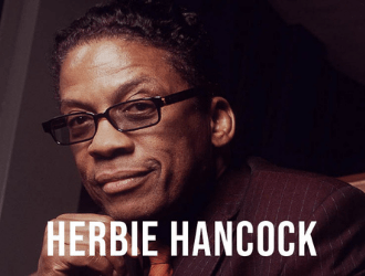 Un hombre que lleva gafas y traje se llama Herbie Hancock.