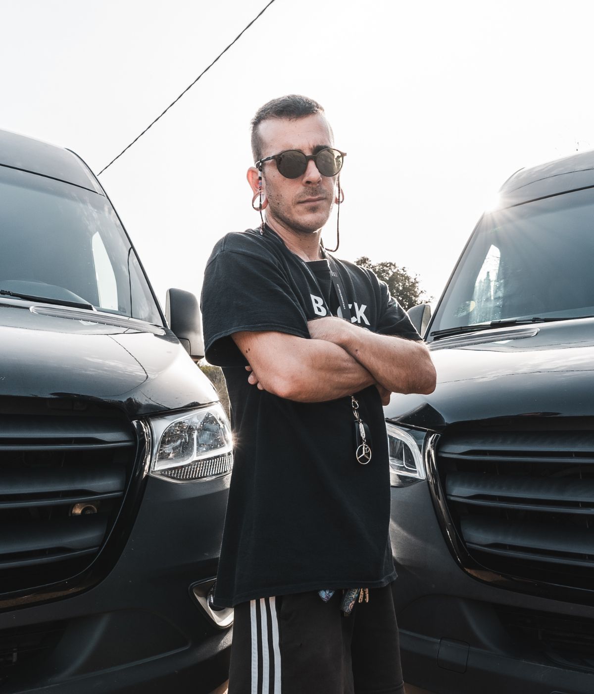 Roberto, CEO de Road Dogs, que lleva gafas de sol está parado delante de dos furgonetas Mercedes Sprinter negras.