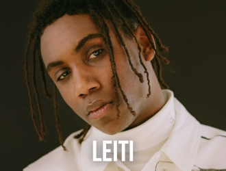 Un joven con rastas lleva una chaqueta blanca con el nombre Leiti.
