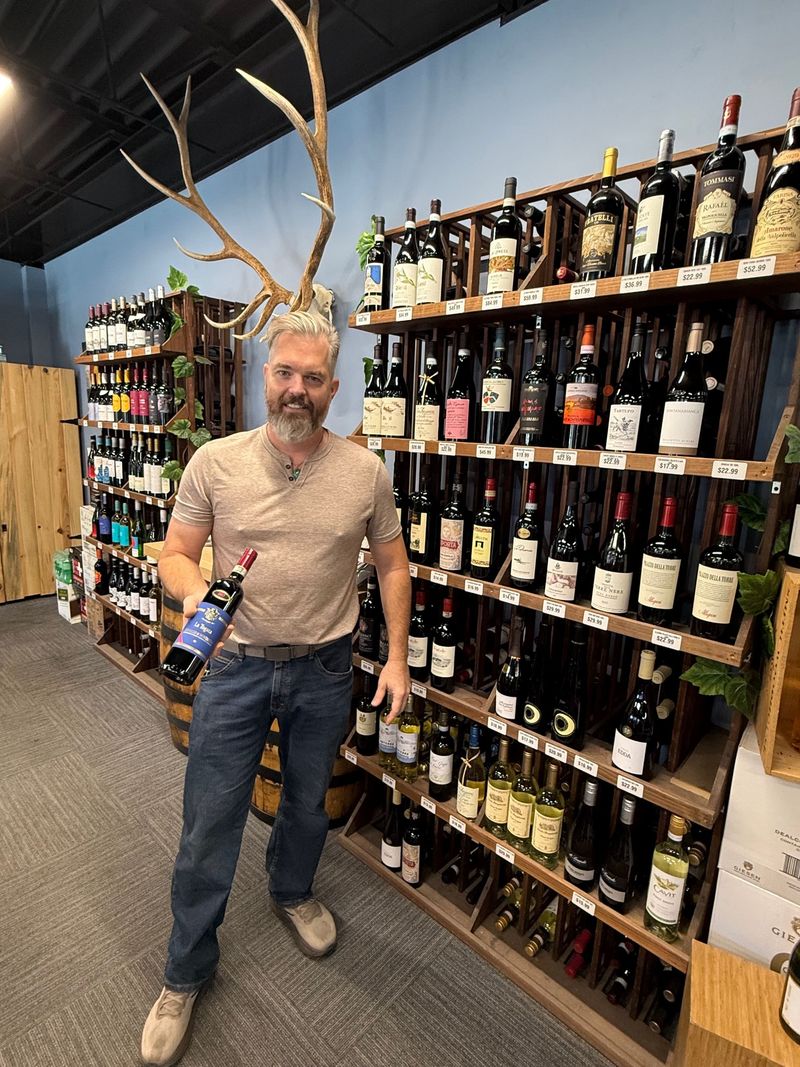 A Pier 13 team member holding a bottle of Italian red in front of the wine wall