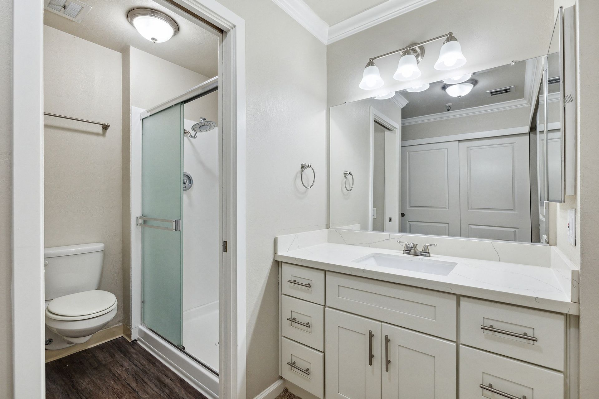 Bathroom in apartment with white vanity, large mirror, and glass shower enclosure at Tower apartments in Alameda, CA.