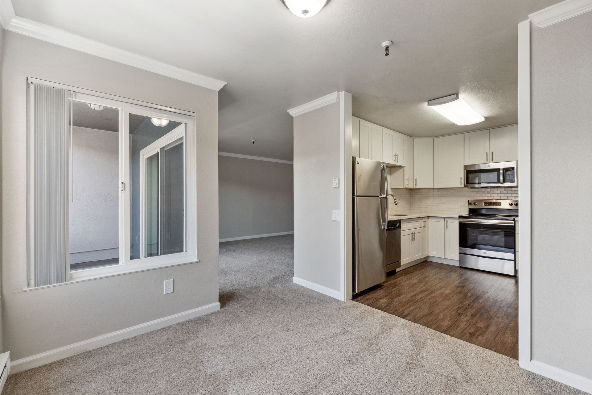 Open living area with carpet and a modern kitchen with stainless steel appliances at Tower apartments in Alameda, CA.