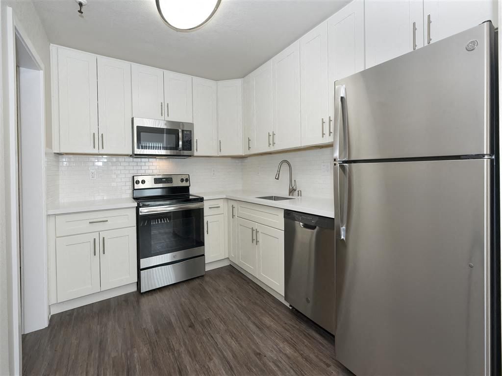 Modern white kitchen with stainless steel fridge, range, microwave, and dishwasher at Tower apartments in Alameda, CA.