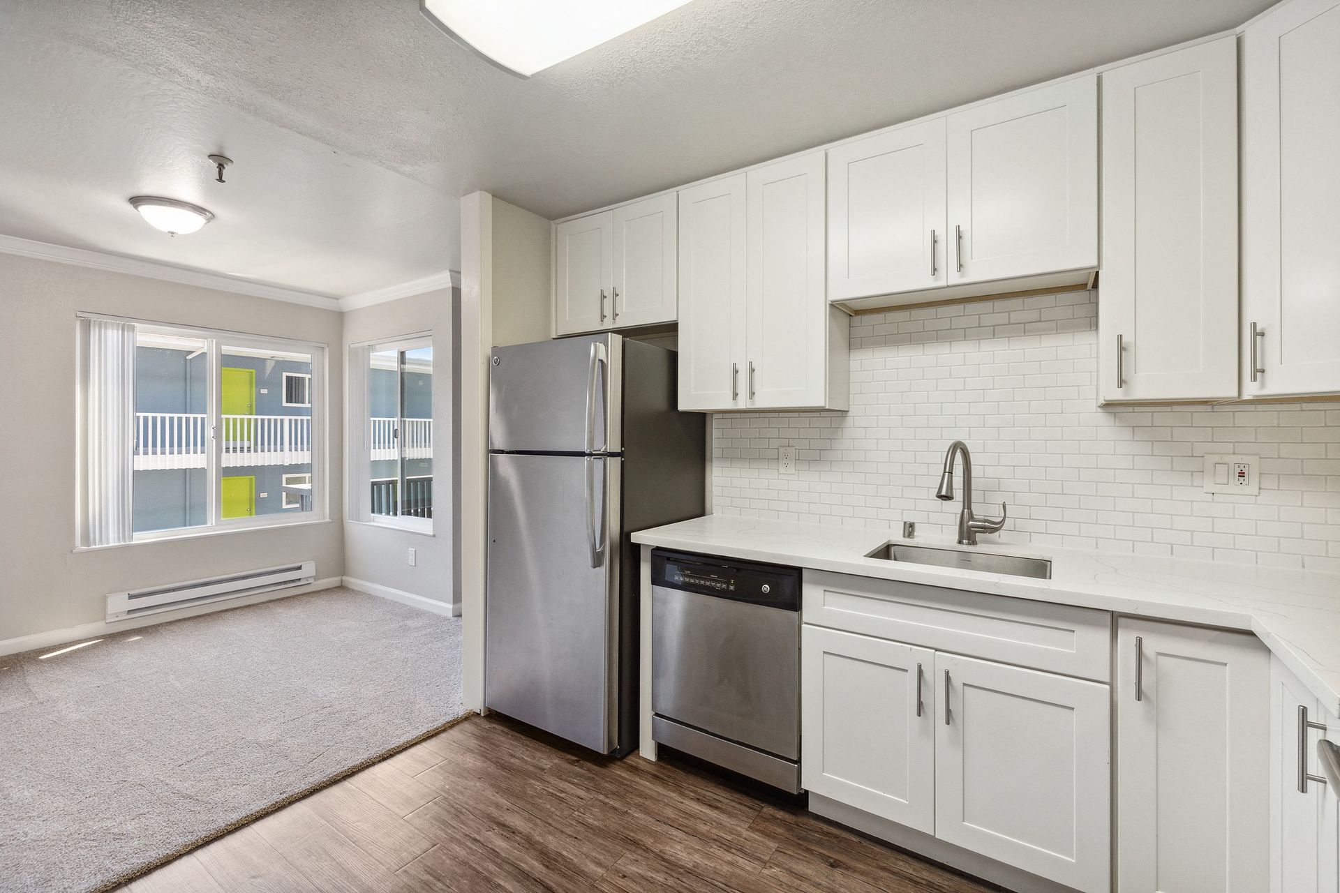 Modern apartment kitchen with white cabinets, stainless steel fridge and dishwasher, and a subway tile backsplash at Tower apartments in Alameda, CA.