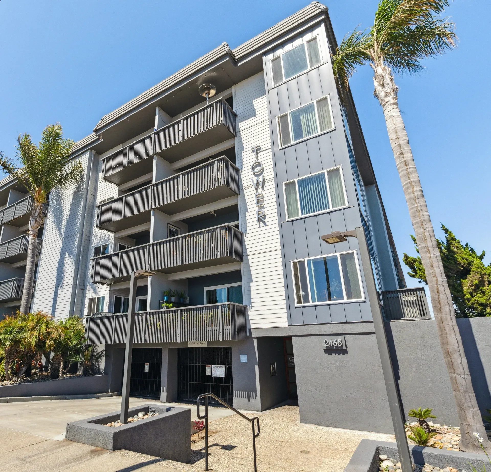 Exterior view of a modern apartment building with balconies and palm trees against a clear blue sky at Tower apartments in Alameda, CA.