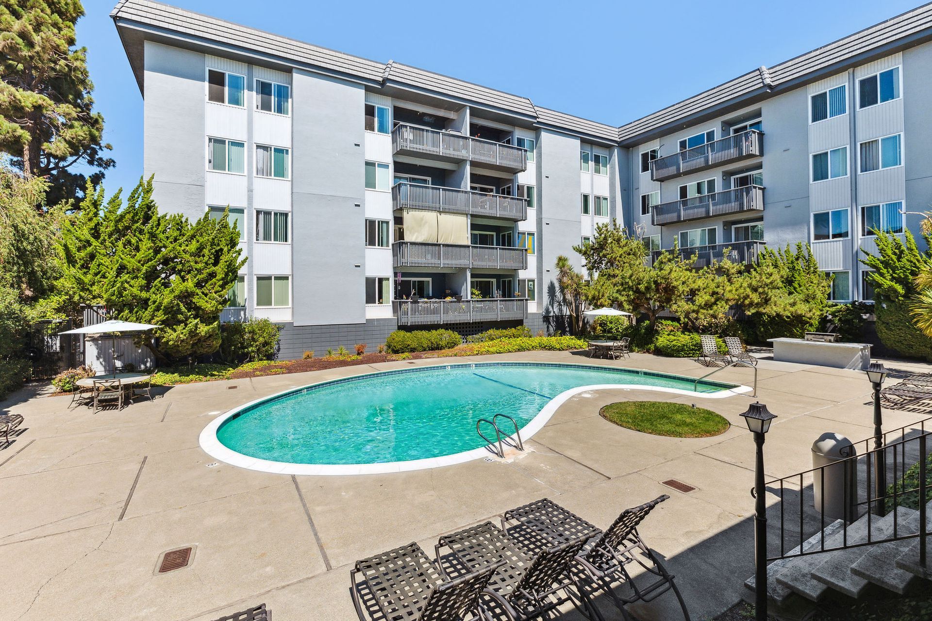 Outdoor pool area in a courtyard with lounge chairs and a gray apartment building at Tower apartments in Alameda, CA.