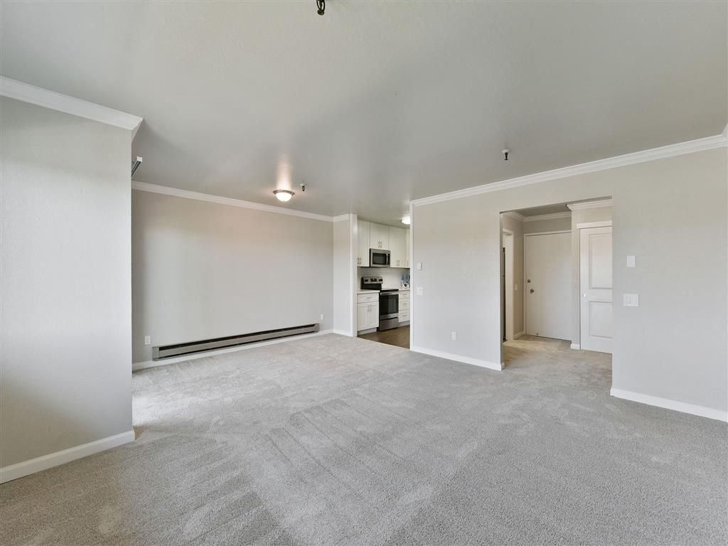 Living room with beige carpet, neutral walls, and an open kitchen at Tower apartments in Alameda, CA.
