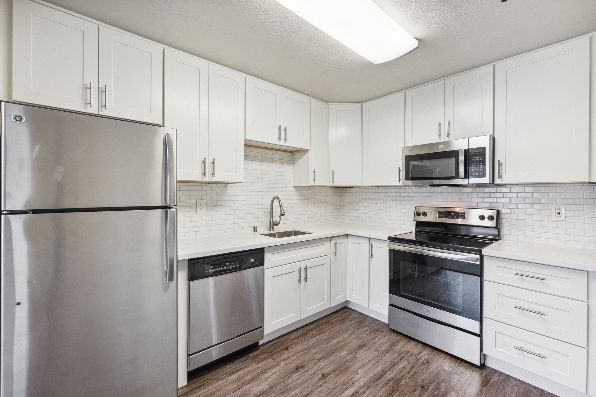 Bright white kitchen with stainless steel fridge, range, microwave, and dishwasher at Tower apartments in Alameda, CA.