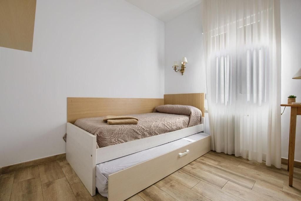 Bedroom with light wood flooring, single bed with trundle, and sheer white curtains.