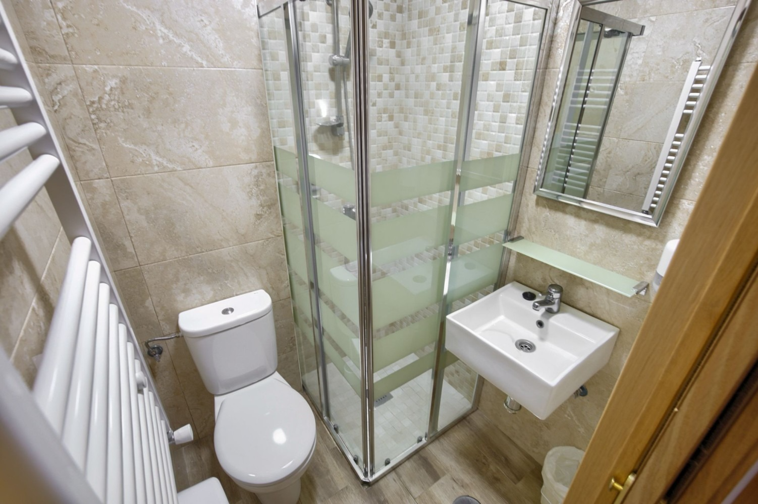 Small bathroom with toilet, shower, and sink; beige tiled walls.