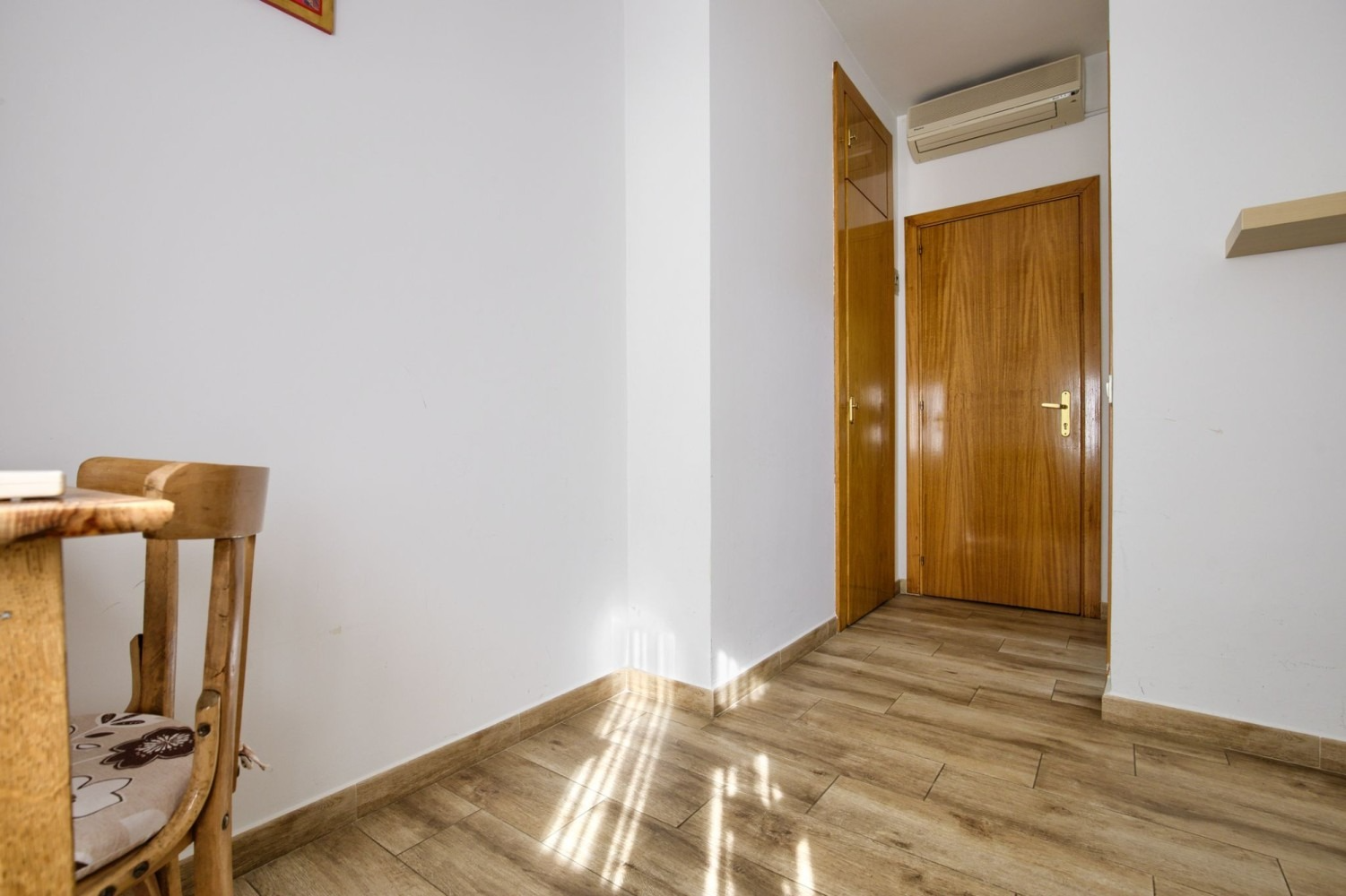Corner of room with wooden floor, white walls, and a closed wooden door.