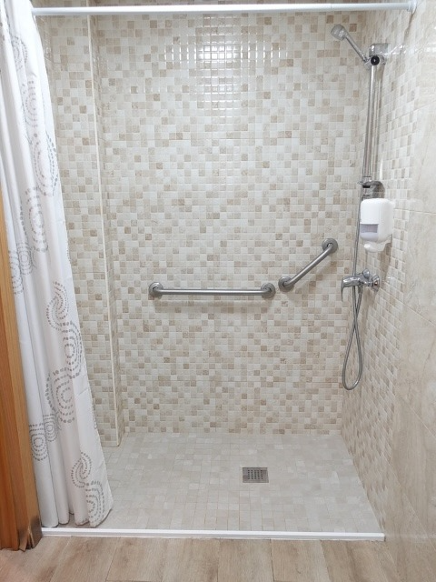 Accessible shower stall with grab bars, tiled walls, and curtain.