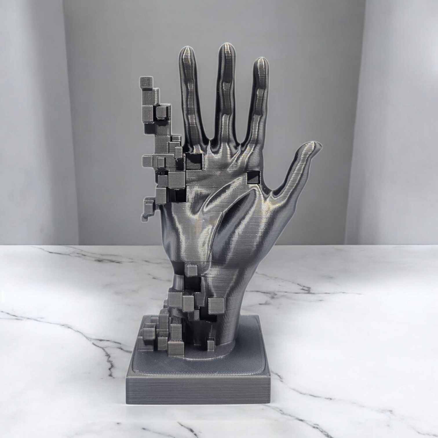 Een metallickleurige, 3D-geprinte handsculptuur waarvan de linkerkant lijkt op te lossen in een verzameling zwevende kubussen.