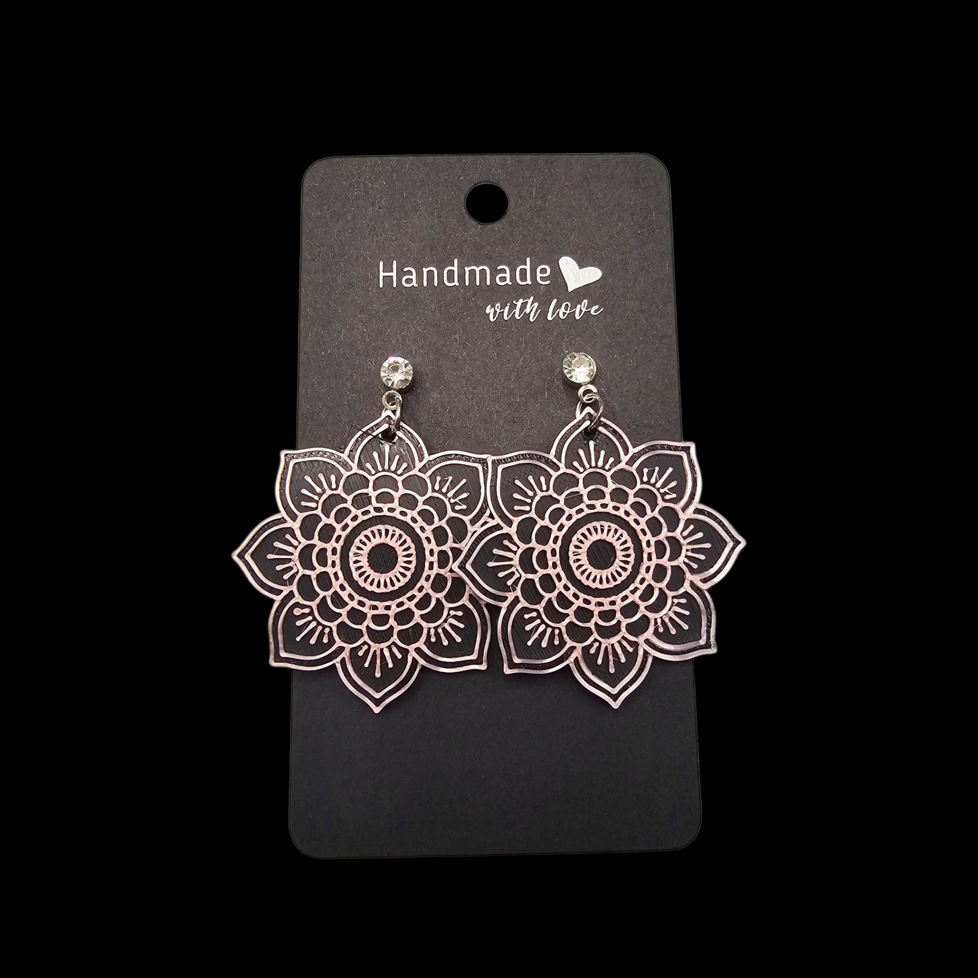 Een paar zilverkleurige, mandala-vormige oorbellen met kleine kristallen, gepresenteerd op een handgemaakt zwart kaartje.