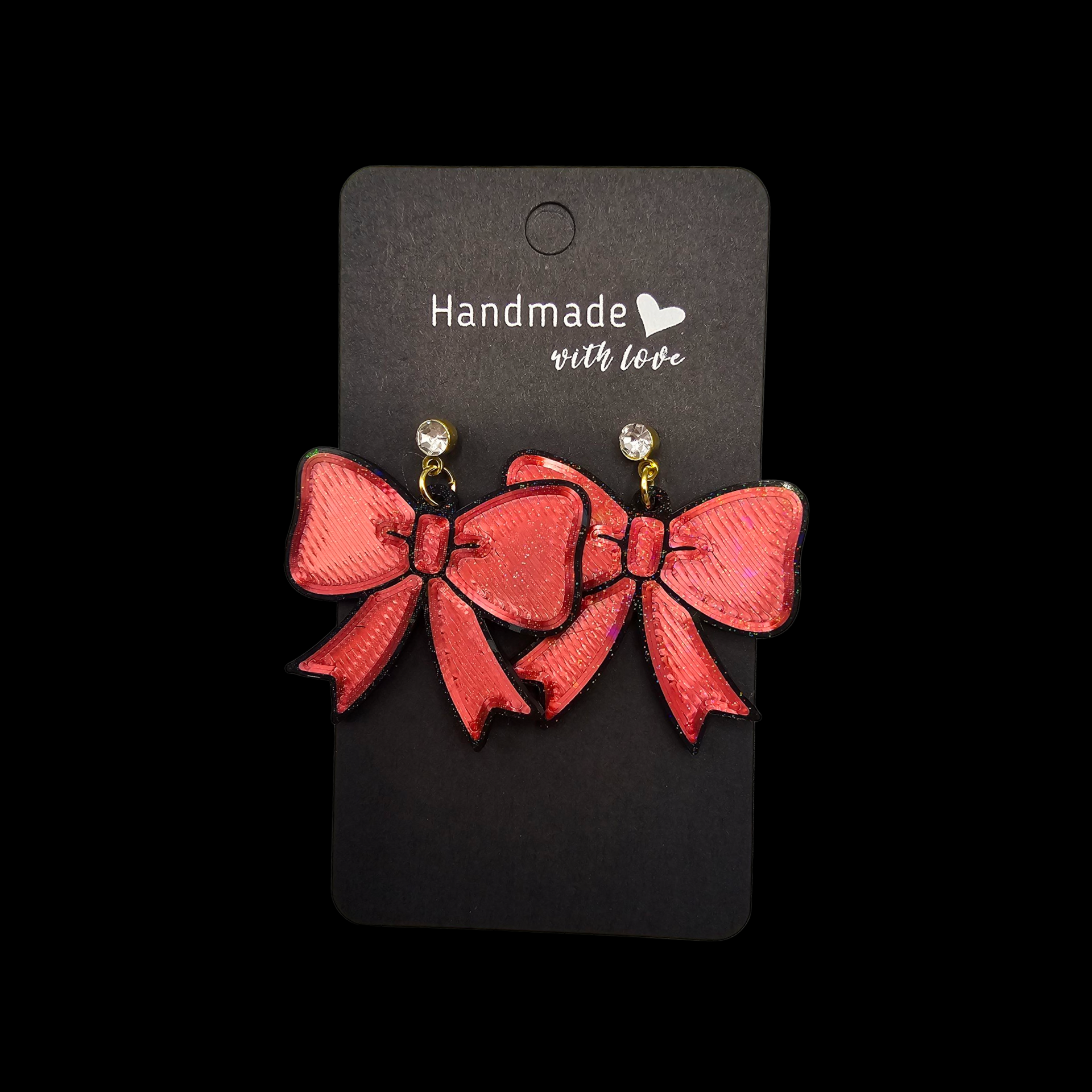 Twee rode stoffen oorbellen met strikjes en kristallen steentjes, gepresenteerd op een zwart kaartje met de tekst "Handgemaakt met liefde".
