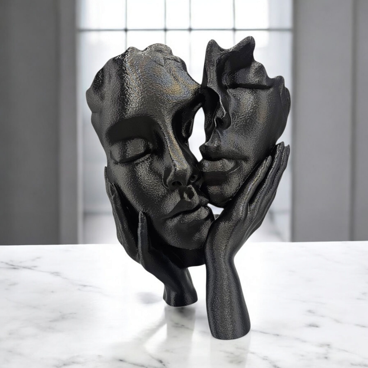 Een zwart, abstract sculptuur met textuur, voorstellende twee gezichten die door twee handen worden vastgehouden, tentoongesteld op een witte marmeren ondergrond.