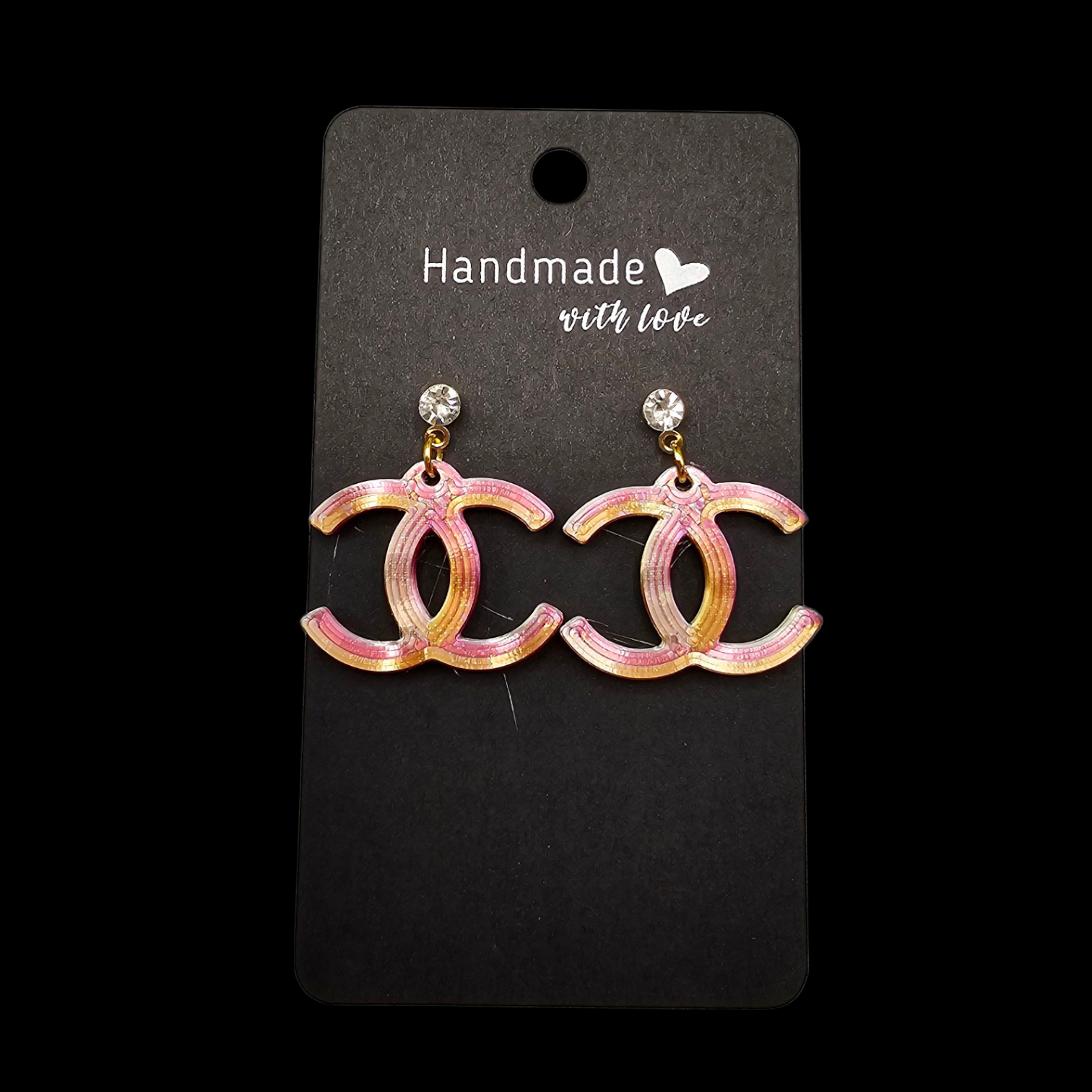 Een paar hangende oorbellen met het CC-logo in een glinsterende roze en oranje kleurovergang op een zwart displaykaartje.